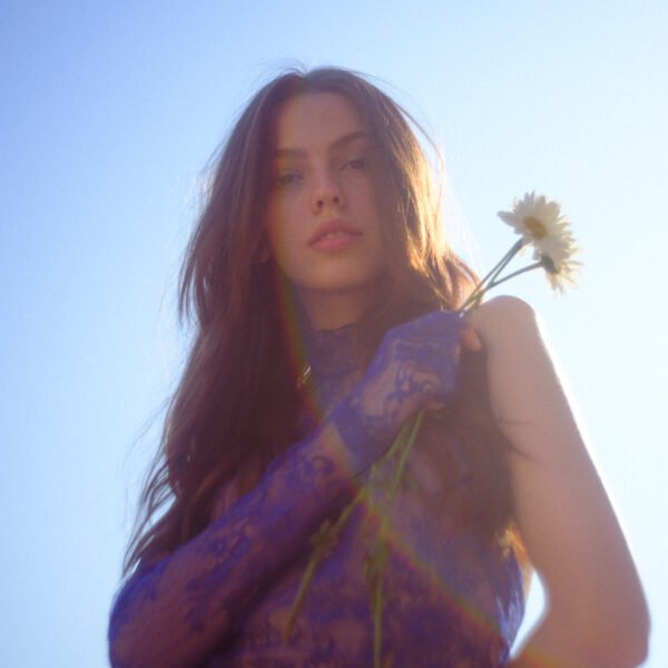 imstillfranci holding a single flower in a blue lace dress, captured in soft natural light with cinematic sun flare.